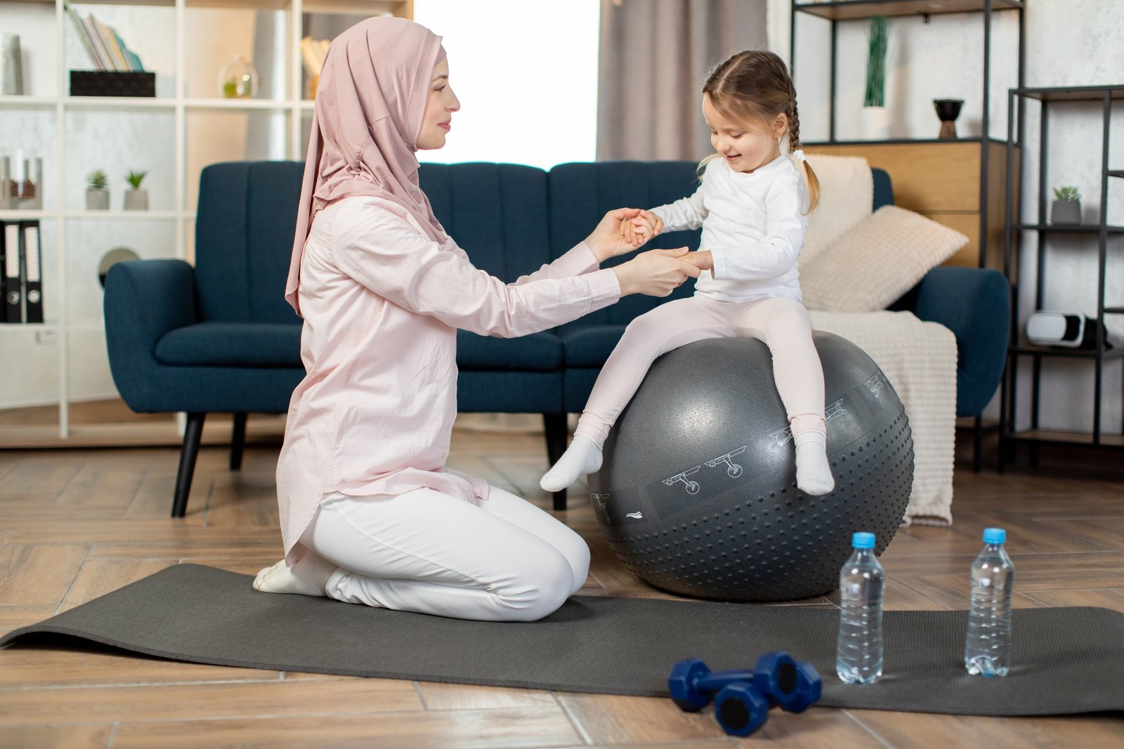 Happy fitness muslim family training on swiss ball in living room.