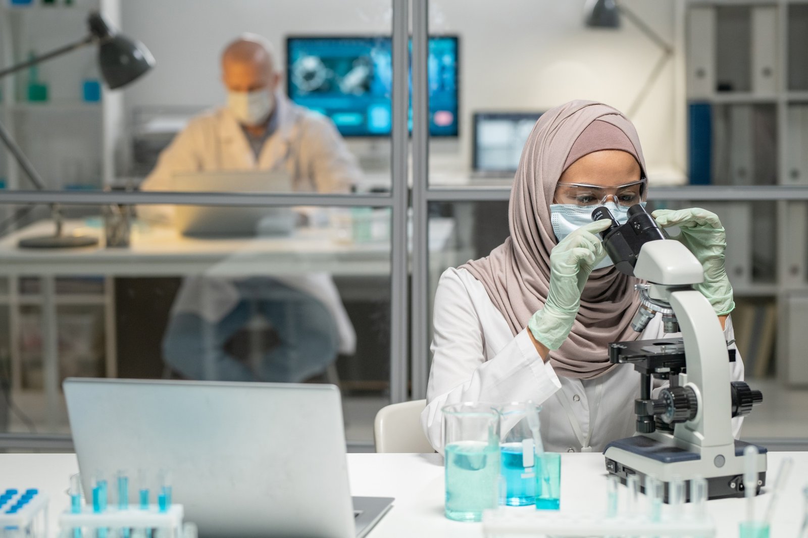 Young Muslim female virologist studying new virus in microscope in laboratory